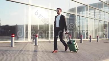 时尚的小胡子戴着太阳镜，带着行李离开机场航站楼，接电话。 商业风格